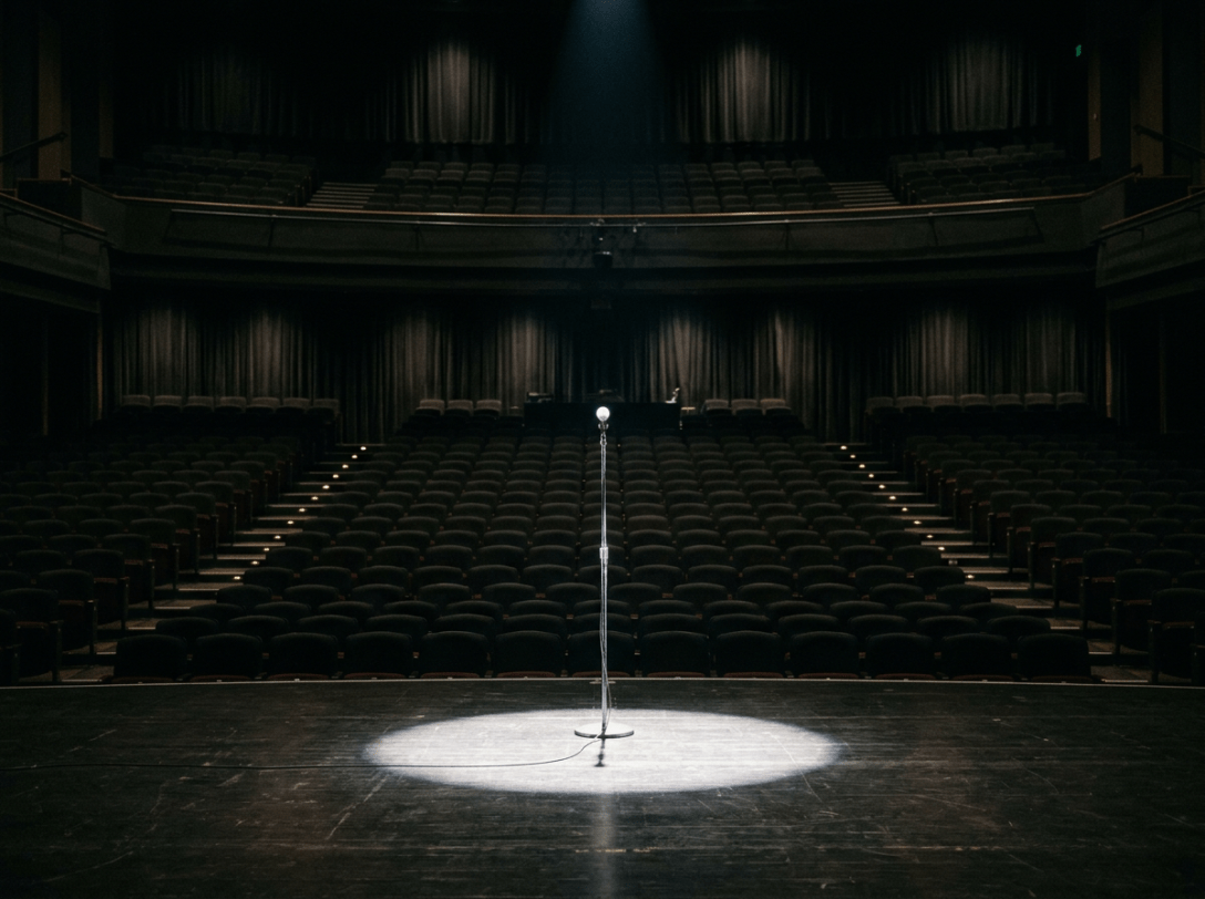 Microphone stand illuminated by a spotlight on an empty theater stage with rows of vacant seats